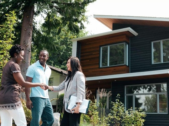 Three people standing outside of a home, smiling and shaking hands.